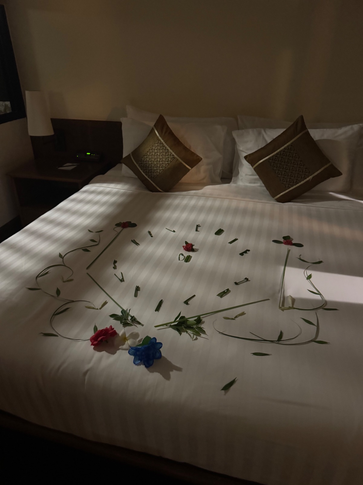 Composition de fleurs et de feuillages disposée sur le lit de la chambre d'hôtel