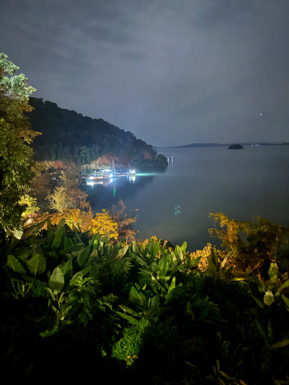 La baie de Phang Nga de nuit au clair de lune, avec les lumières d'un embarcadère au pied de la colline