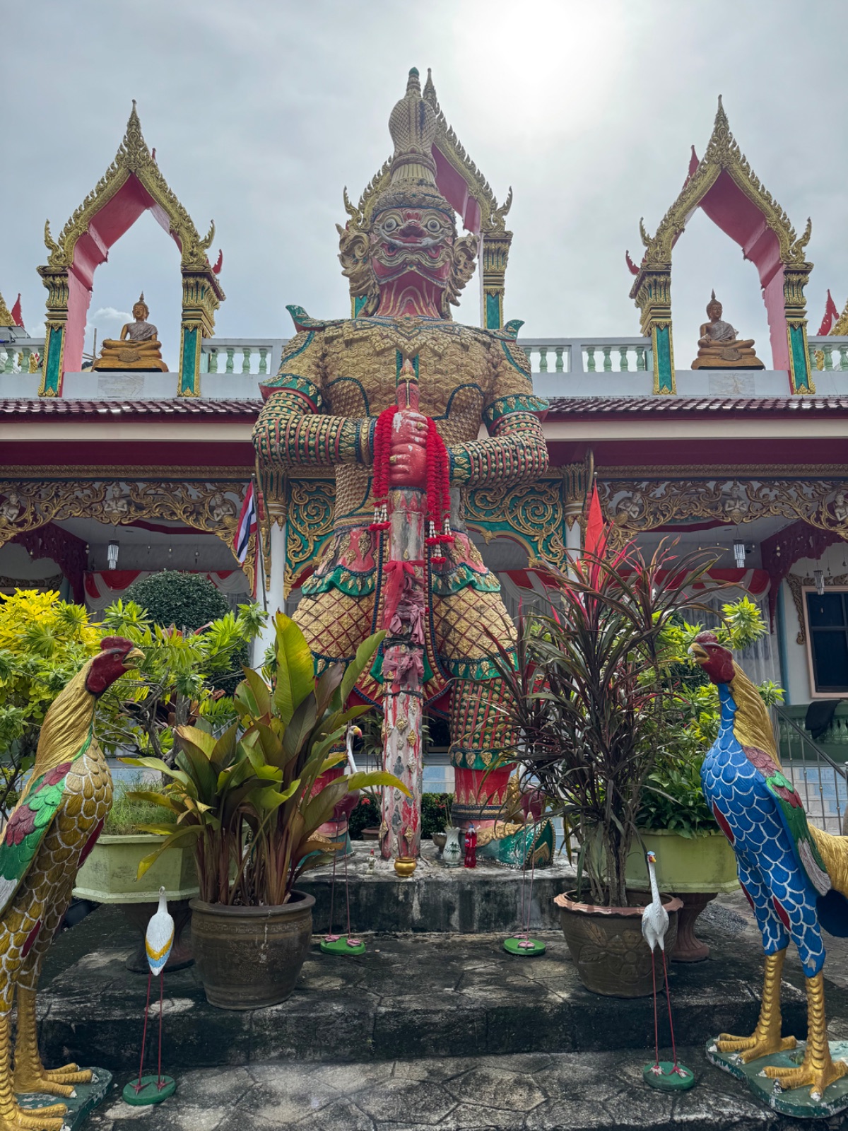 Statue géante de gardien yaksha doré entourée de statues de coqs multicolores au Wat Sri Sunthon
