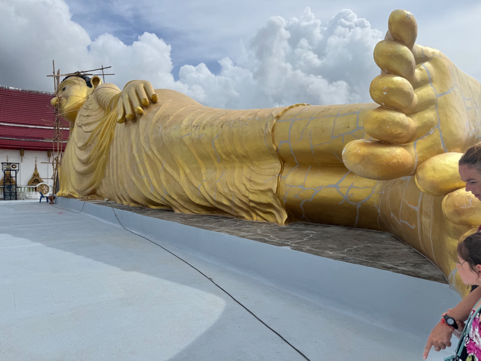 Le Bouddha couché doré de 29 mètres du Wat Sri Sunthon vu depuis ses pieds, sous un ciel de nuages
