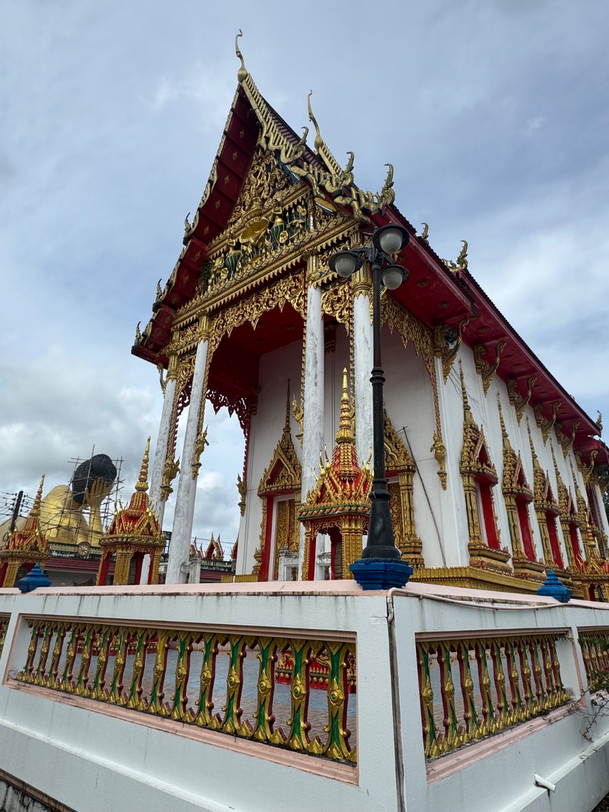 Bâtiment principal blanc, rouge et or du Wat Sri Sunthon à Phuket, avec le grand Bouddha couché visible derrière