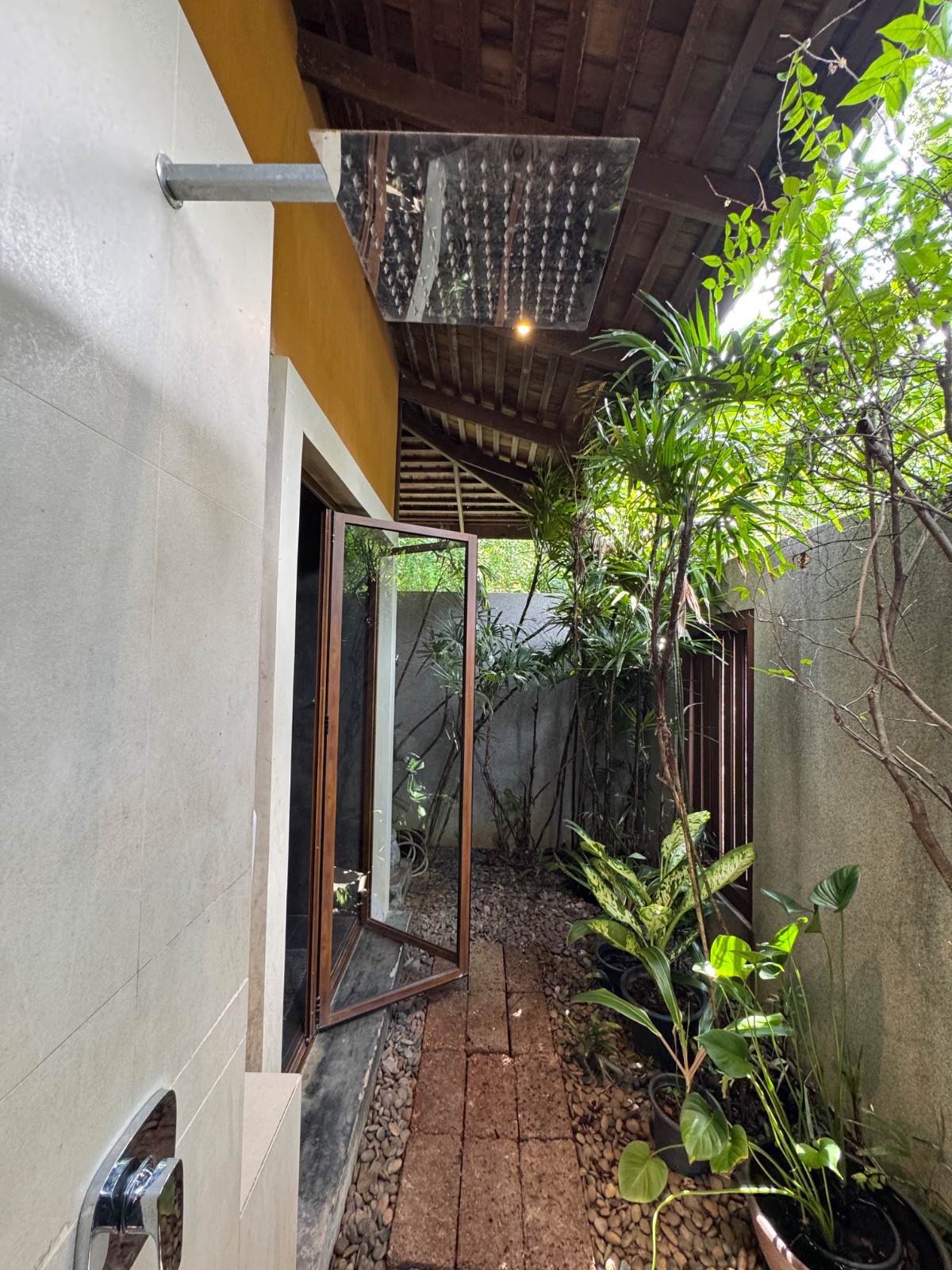 Douche extérieure de la villa, pomme de pluie sous un toit de bois ouvert sur un jardin tropical privé