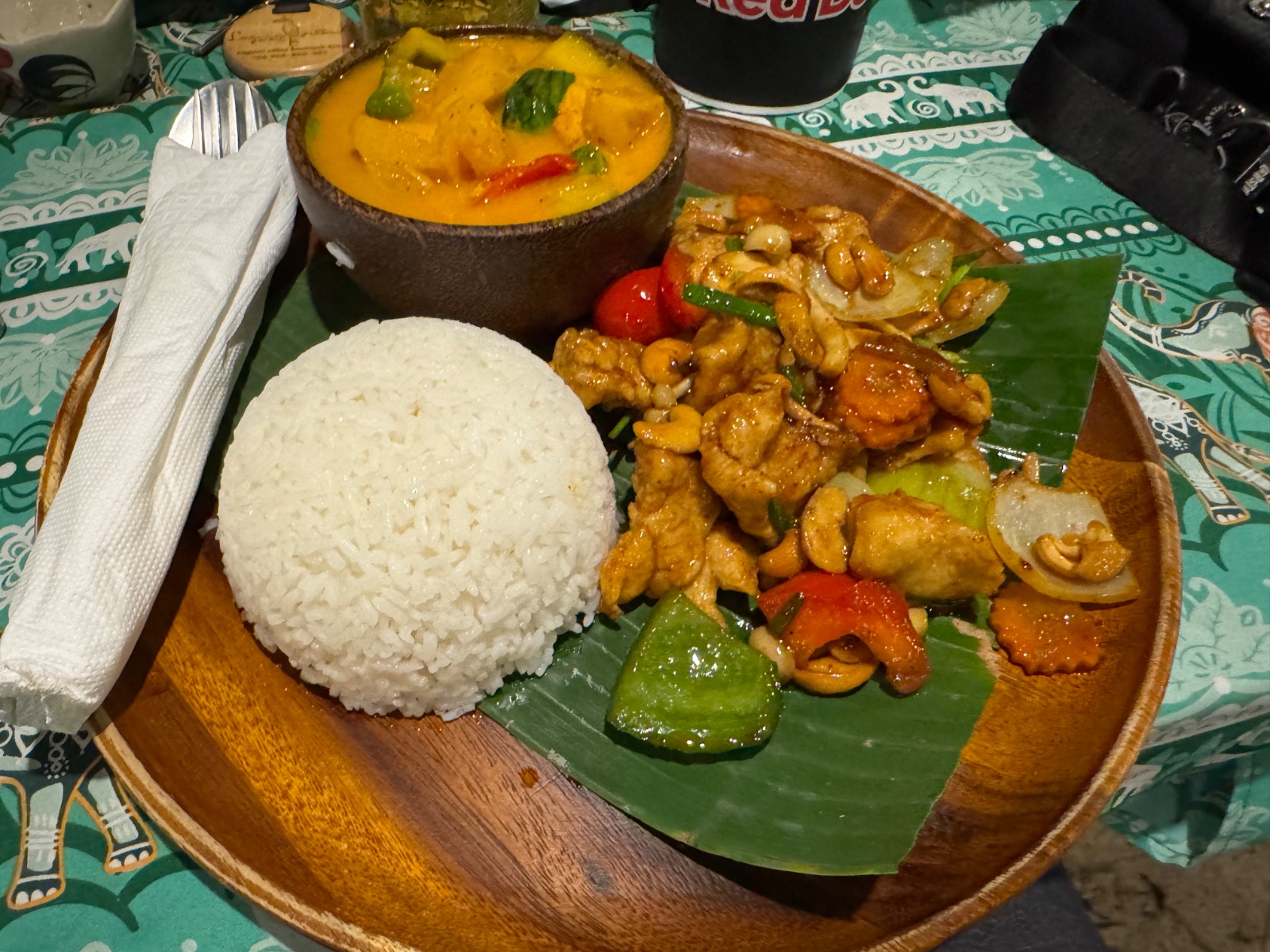Plat thaïlandais servi sur feuille de bananier : poulet aux noix de cajou, riz et curry dans une noix de coco