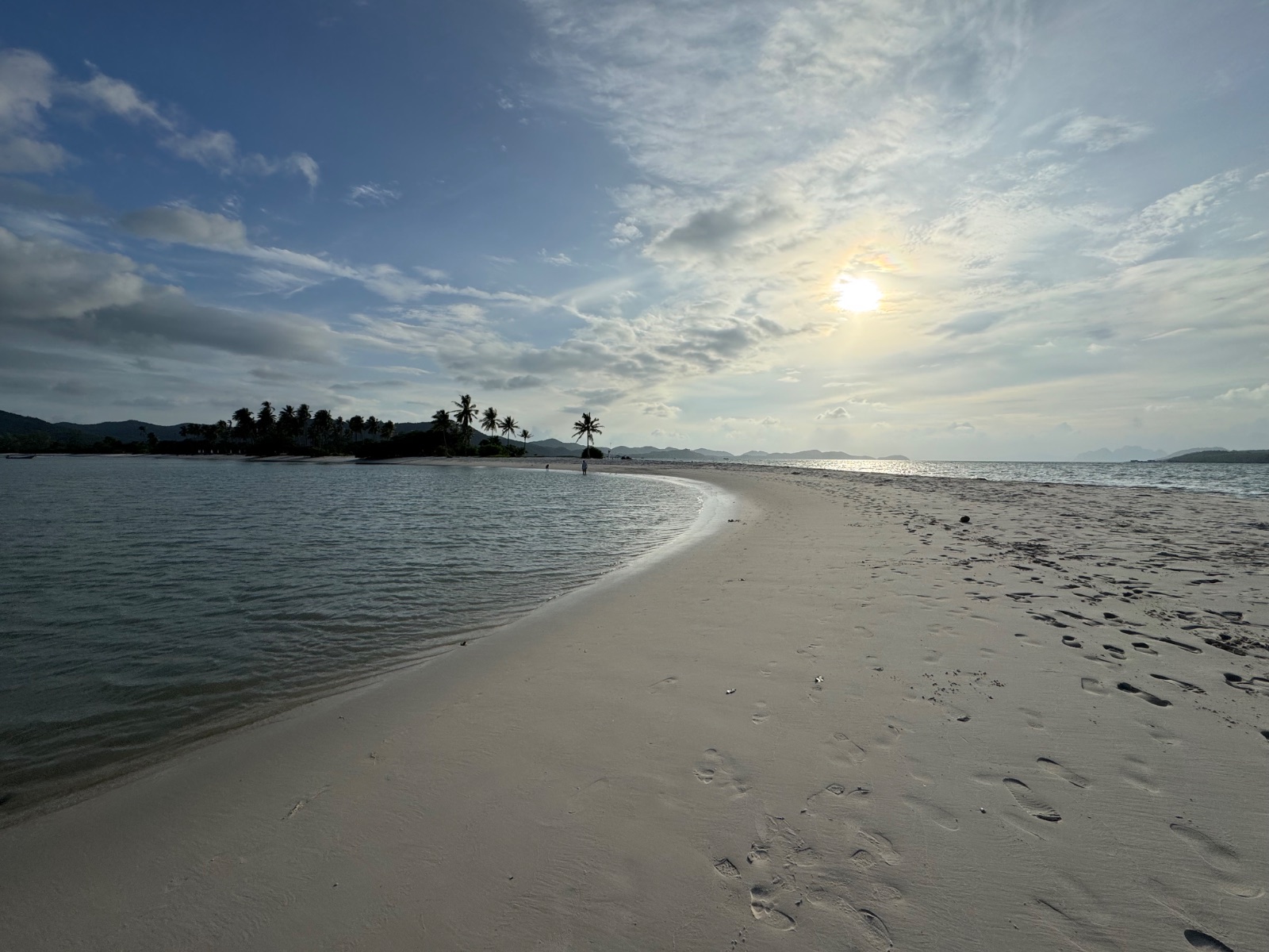 La flèche de sable blanc s'avançant dans la mer entre deux plans d'eau calme, palmiers au loin