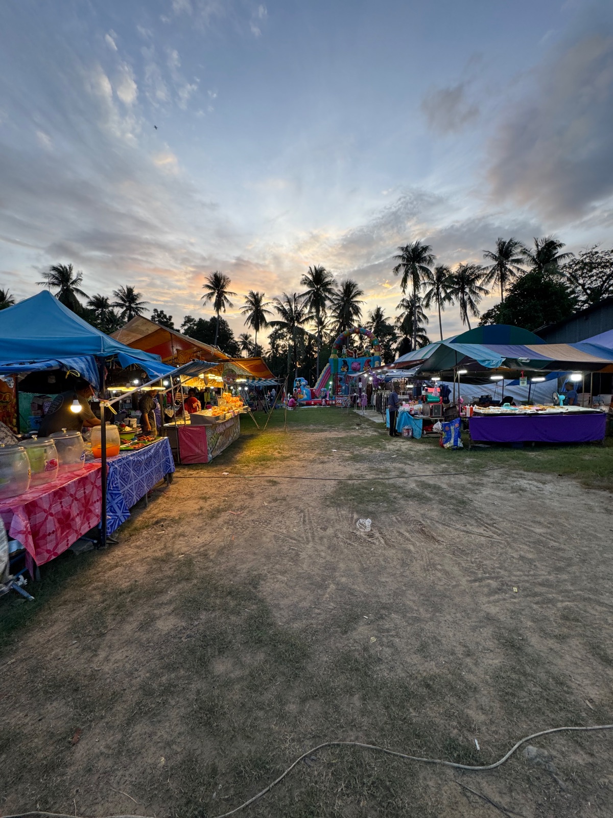 Stands du marché du mercredi soir de Koh Yao Noi sous les palmiers au coucher du soleil, château gonflable au fond