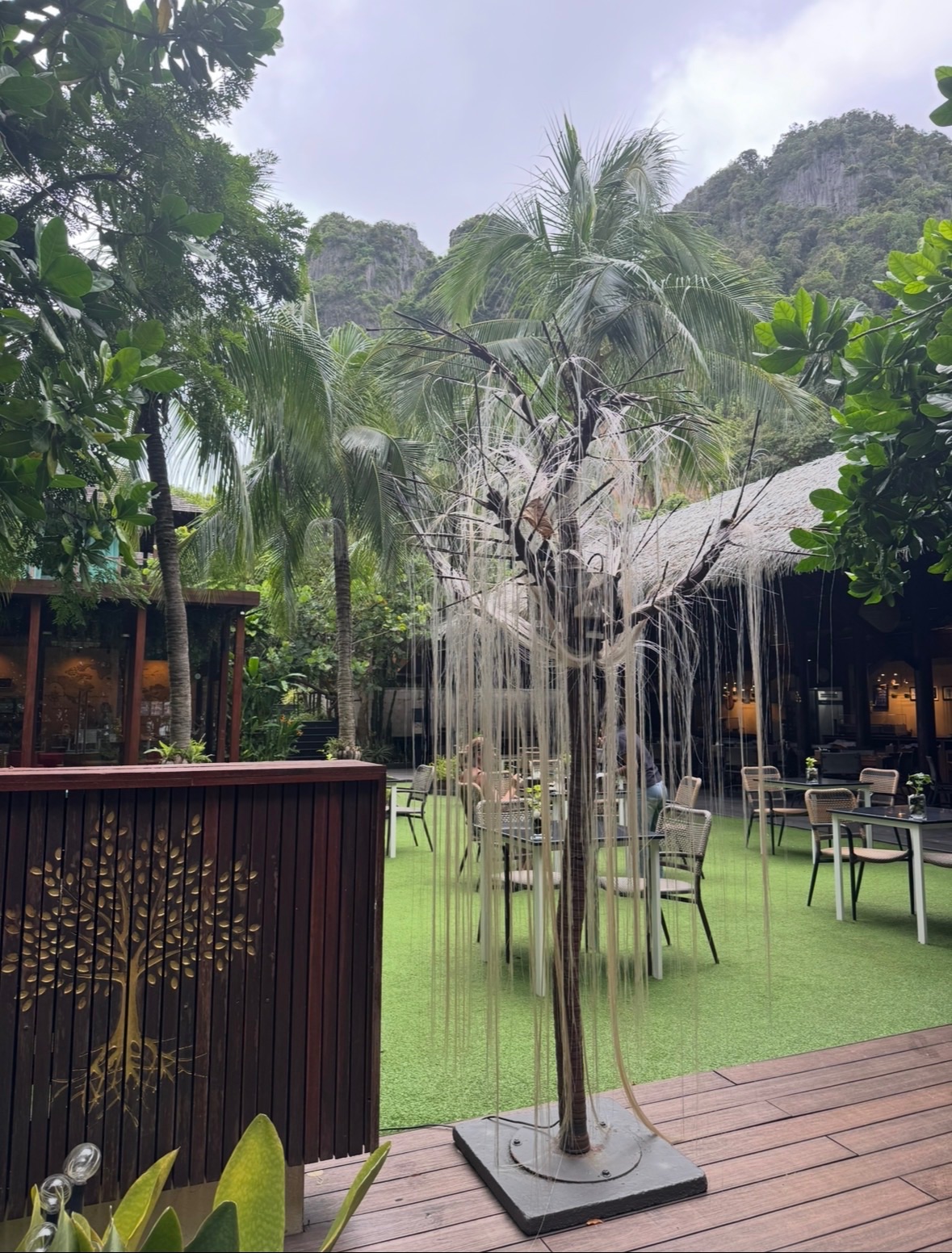 Le jardin du restaurant Avatar Railay, avec ses tables sur pelouse, son arbre décoratif et les falaises karstiques en fond