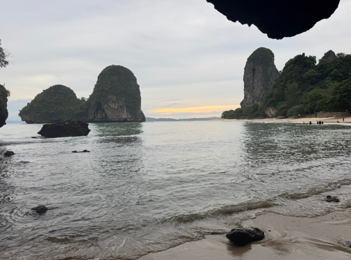Coucher de soleil sur la plage de Phra Nang, vu depuis l'abri d'un surplomb rocheux, avec les pitons karstiques se découpant sur le ciel orangé