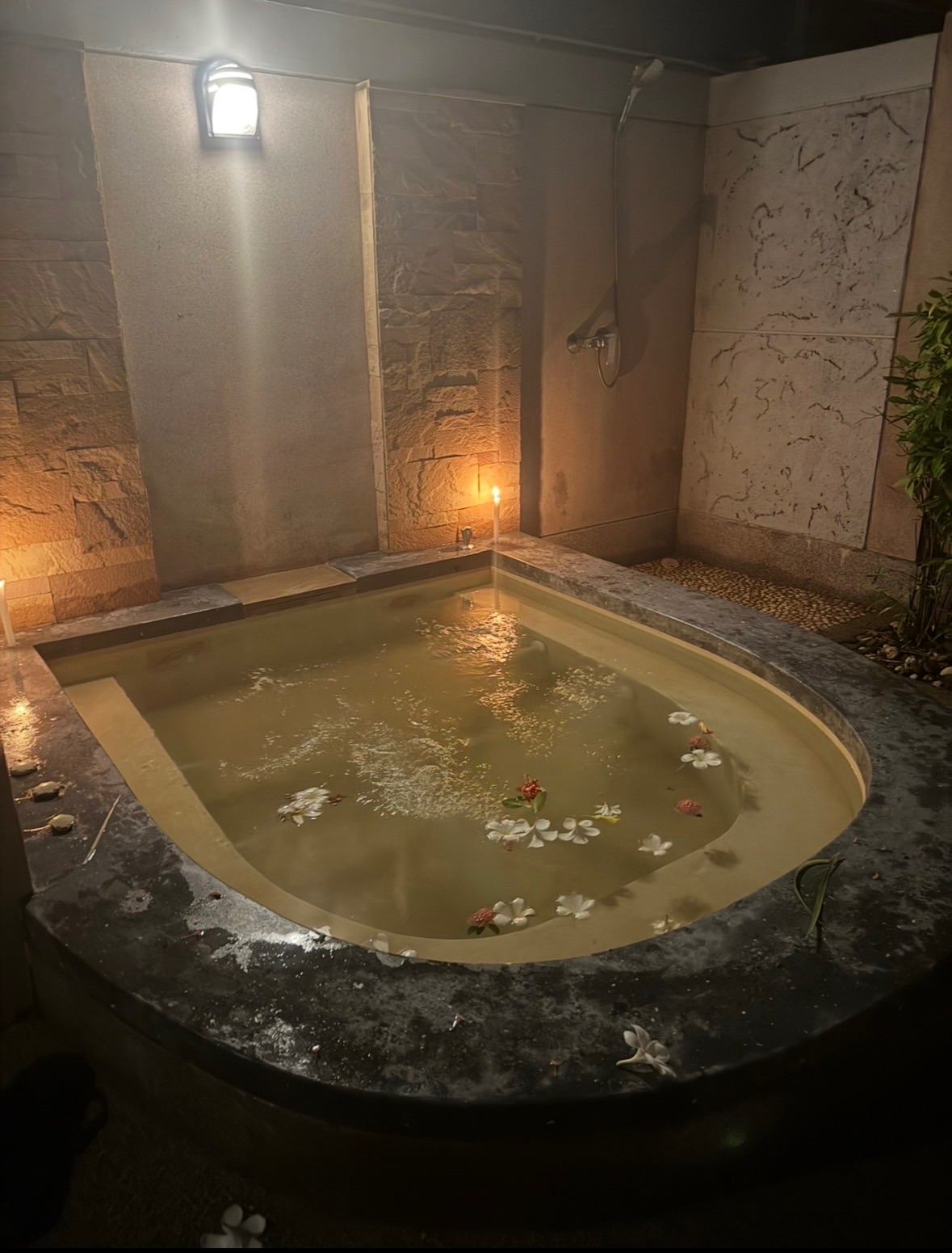 Le bassin de la villa transformé en spa maison, avec des pétales de frangipanier flottants et des bougies allumées autour, à la nuit tombée
